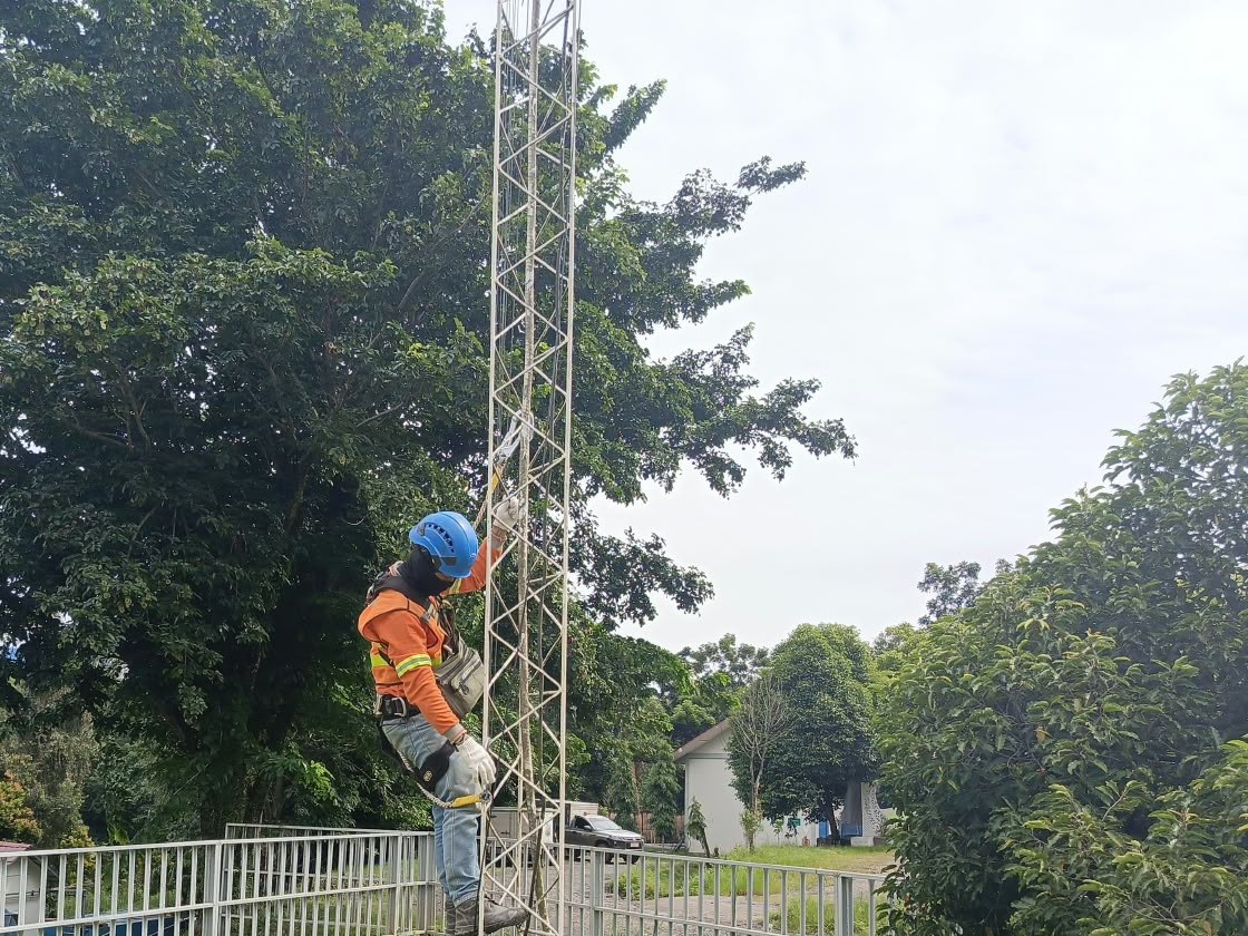 Teknisi bersabuk pengaman memasang perangkat di menara jaringan site PAMA